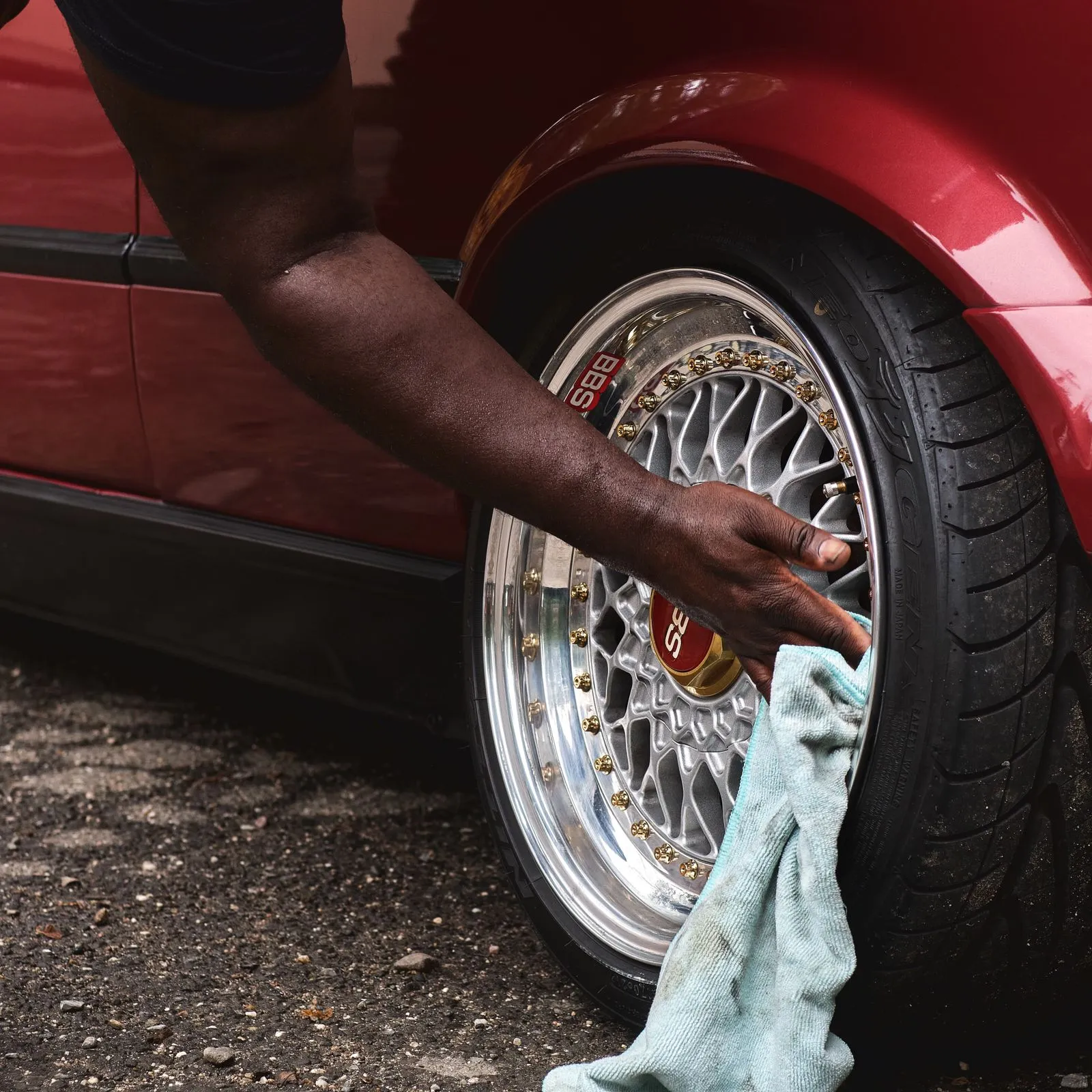 A detailer wiping a polished wheel on a red car with a microfibre cloth