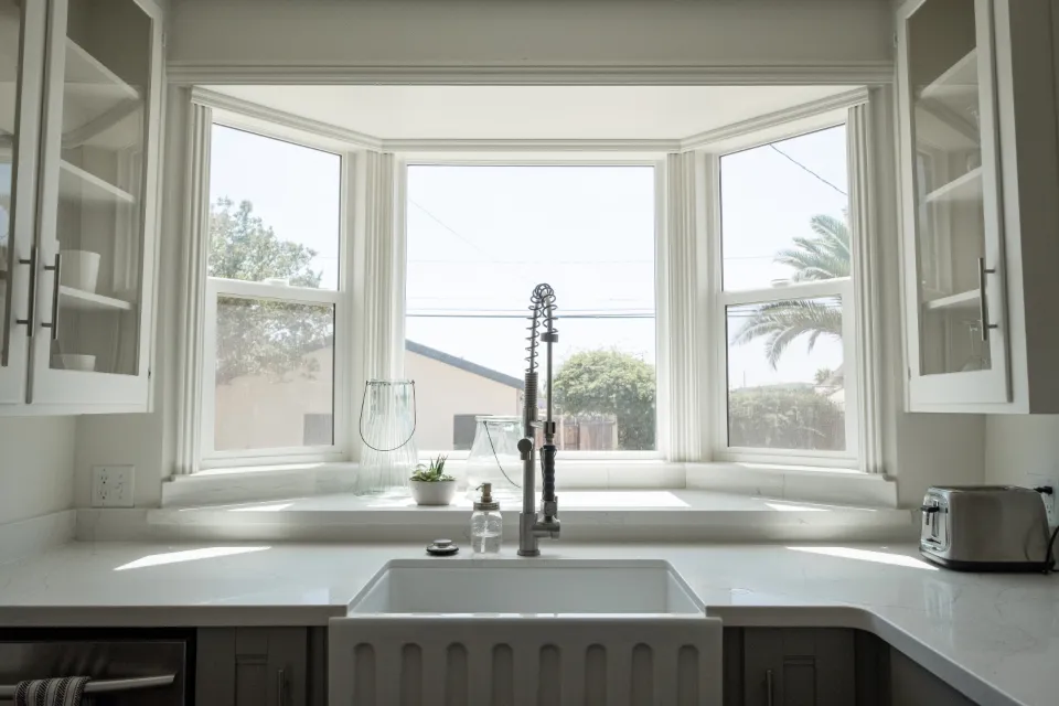 A kitchen bay window with three white frames above the sink